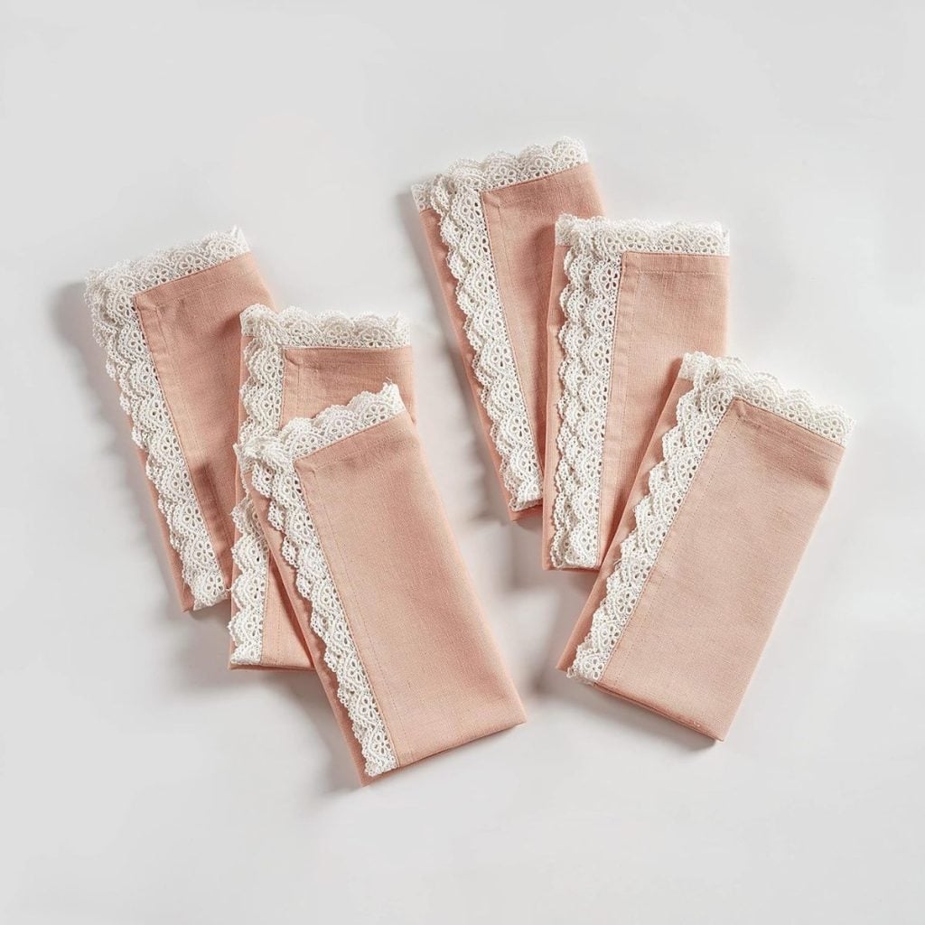 Six folded pink cloth napkins with white lace trim, perfect as Valentine table decorations, arranged on a white background.