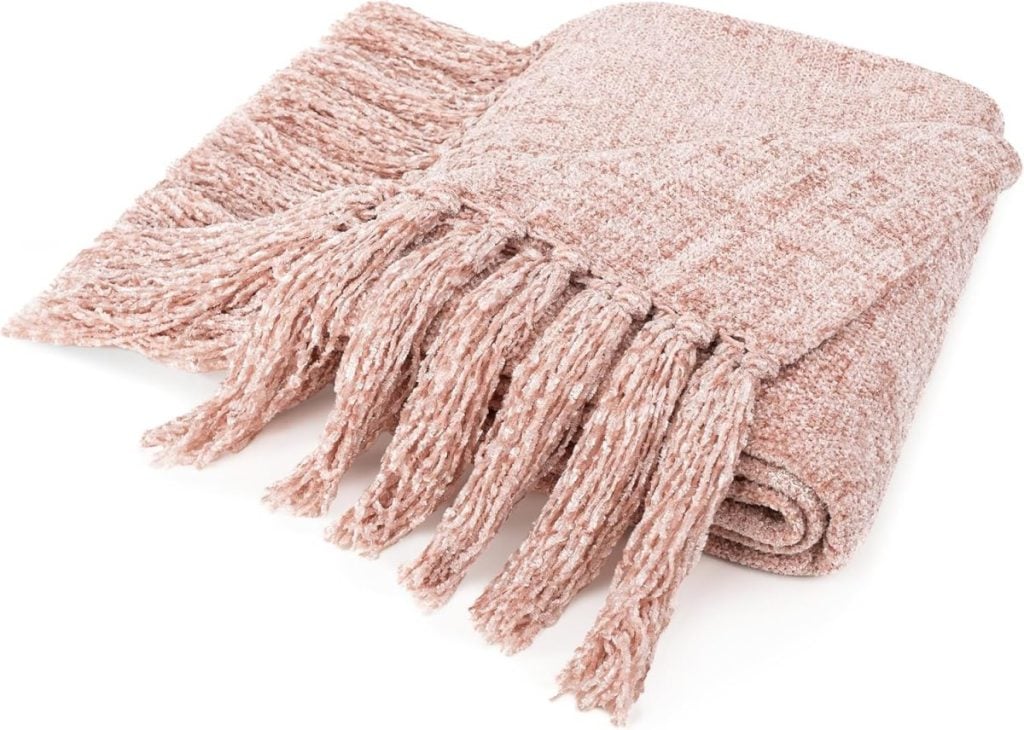 A folded, textured pink blanket with fringe tassels on one end.