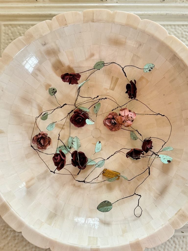 A decorative bowl with a string of artificial roses and green leaves placed inside, viewed from above.