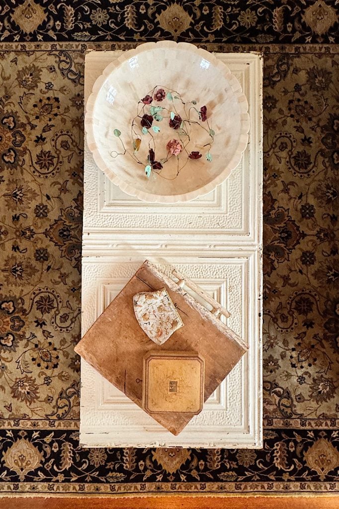 Ornate rug beneath a white table holding a decorative bowl with flowers, a worn book, and patterned paper.