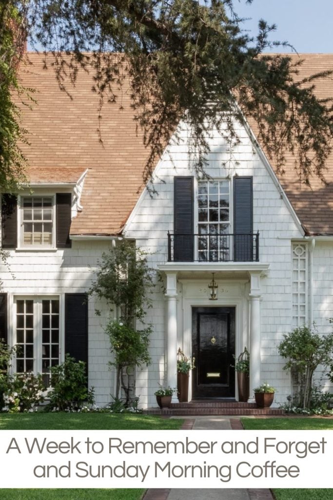 A classic two-story house with white siding and black shutters, featuring a central door and small porch, surrounded by greenery.