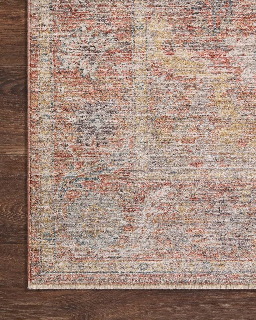 A close-up view of a multicolored woven rug with abstract patterns in shades of orange, brown, and cream on a dark wooden floor.