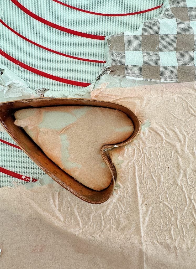 Heart-shaped cookie cutter on rolled dough with a checkered cloth nearby.