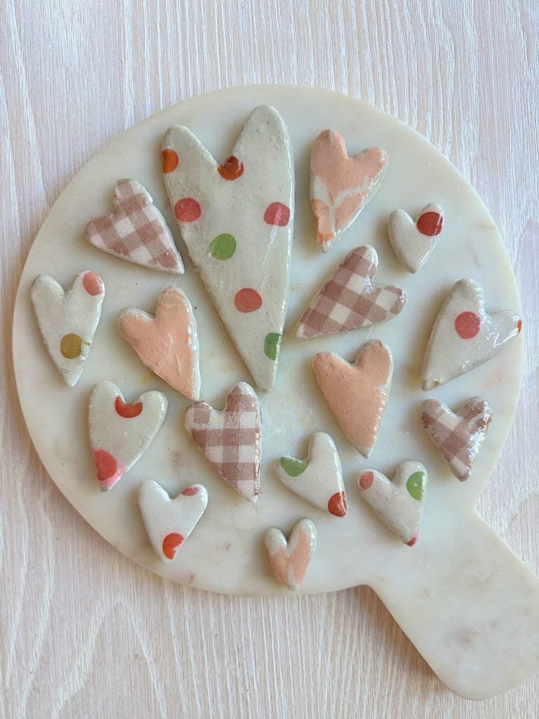 Wooden board with various pastel-colored, heart-shaped cookies, featuring polka dot and checkered patterns.