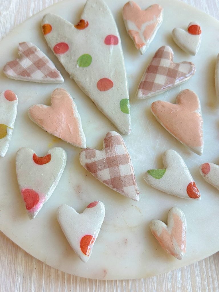 A collection of heart-shaped clay pieces decorated with polka dots and checkered patterns, displayed on a round white surface.