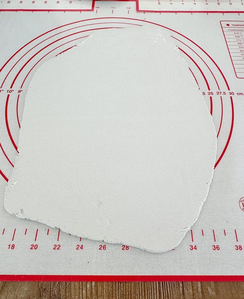 A piece of white fondant is rolled out on a red and white measurement mat.