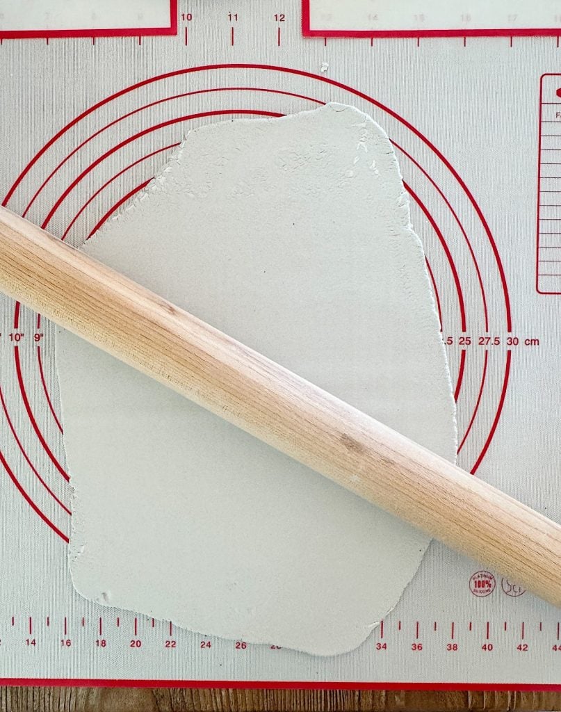 A wooden rolling pin on partially rolled-out dough on a silicone pastry mat with measurement markings.