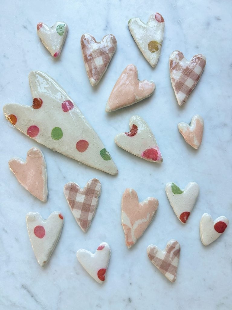 Collection of clay hearts in various sizes with polka dot and gingham patterns on a marble surface.