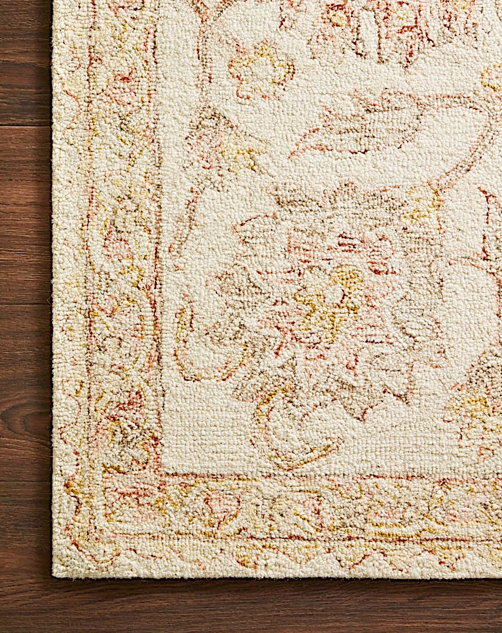 Close-up of a beige carpet with a floral pattern in red and yellow hues on a wooden floor.