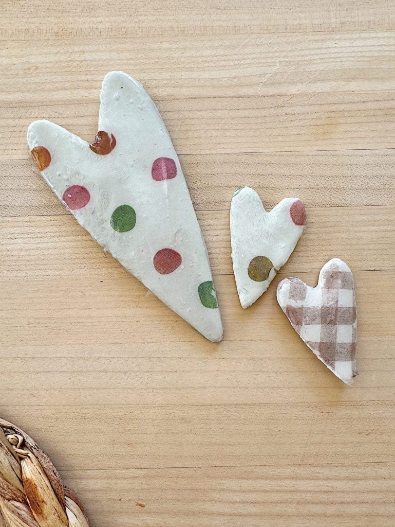 Three heart-shaped clay pieces with different patterns: large with colorful dots, medium with green accents, and small with a gingham pattern, on a wooden surface.