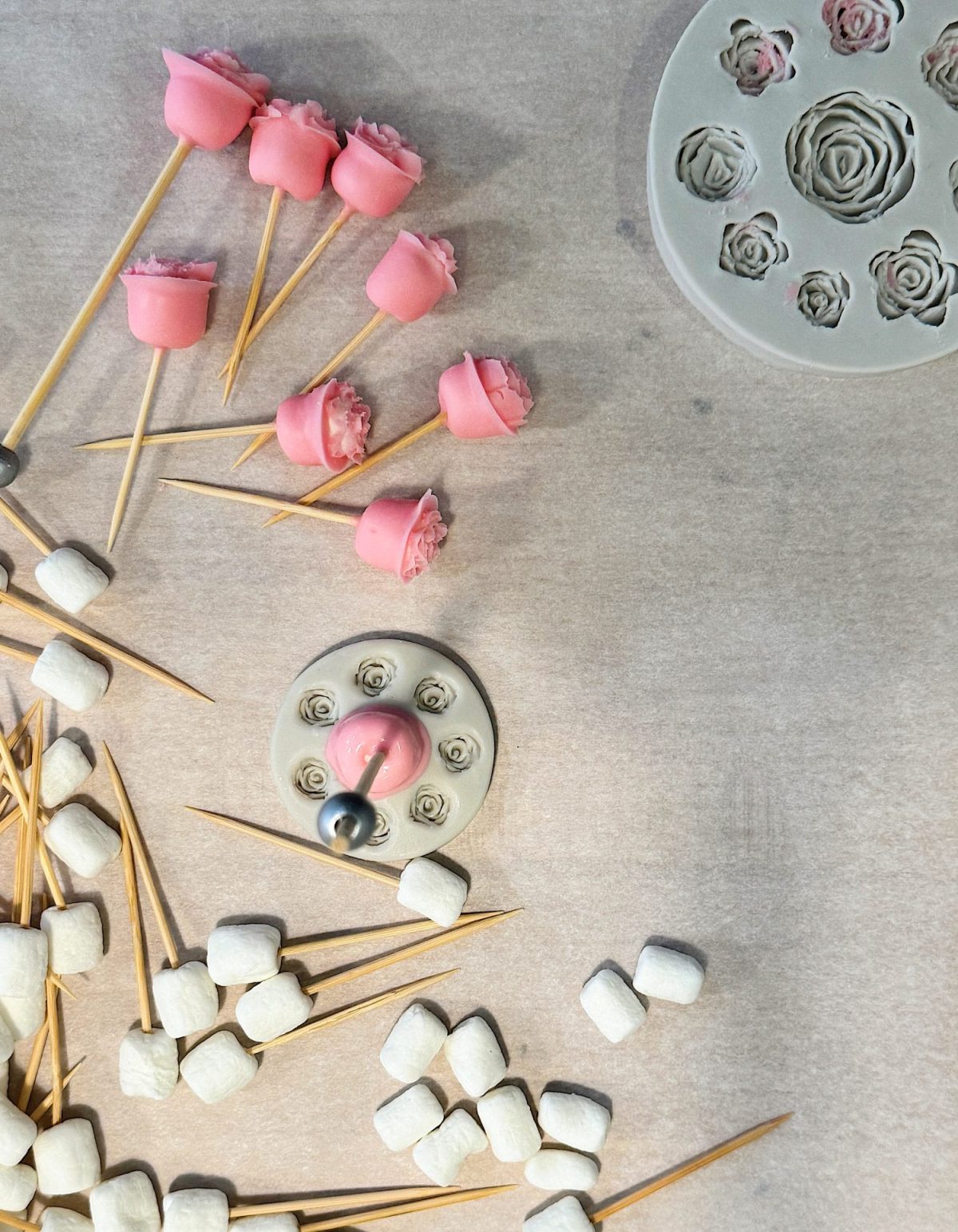 Assorted pink and white fondant decorations, including roses on sticks, with molds on a gray surface.