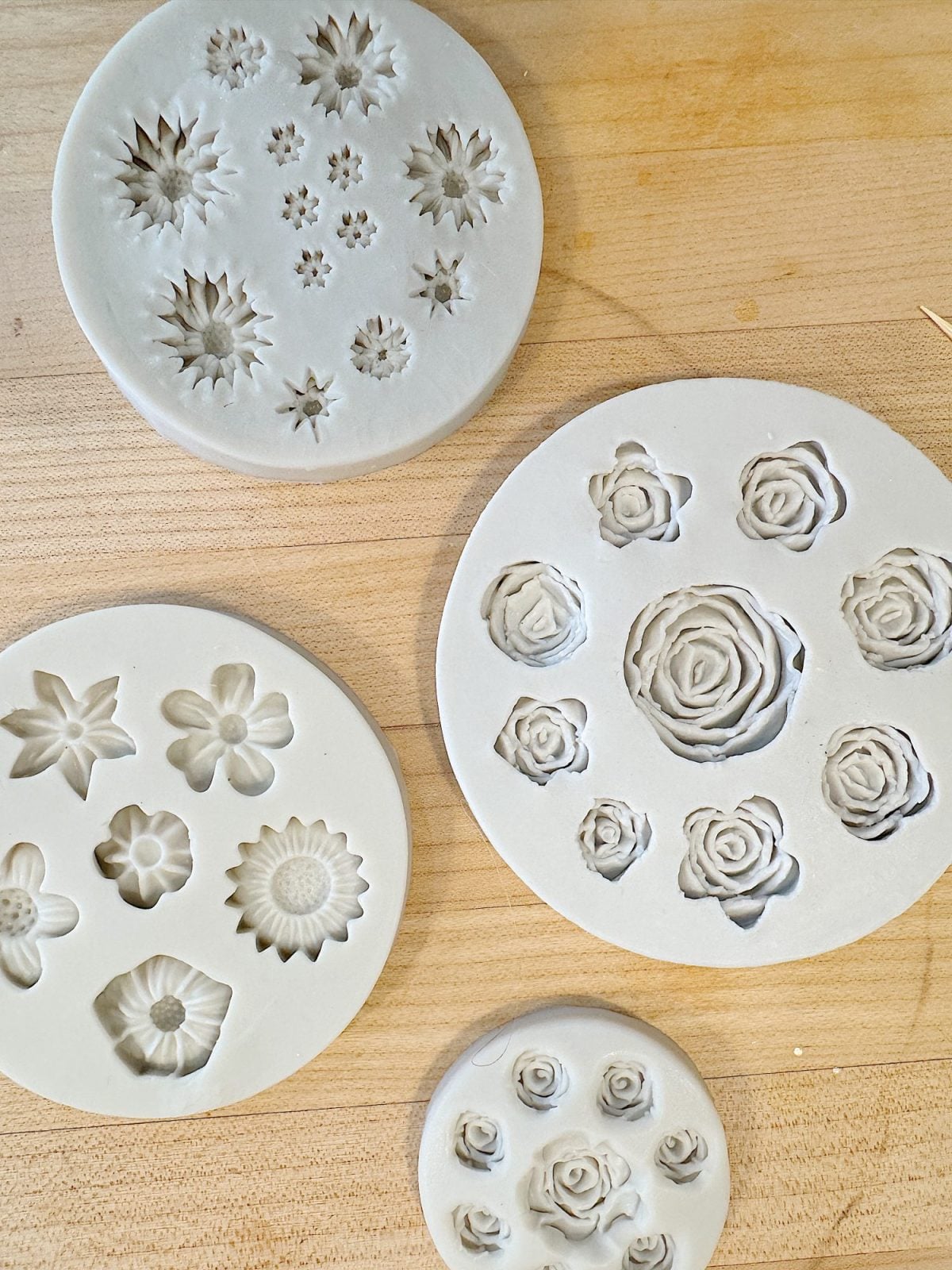 Four circular silicone molds with floral patterns on a wooden surface.