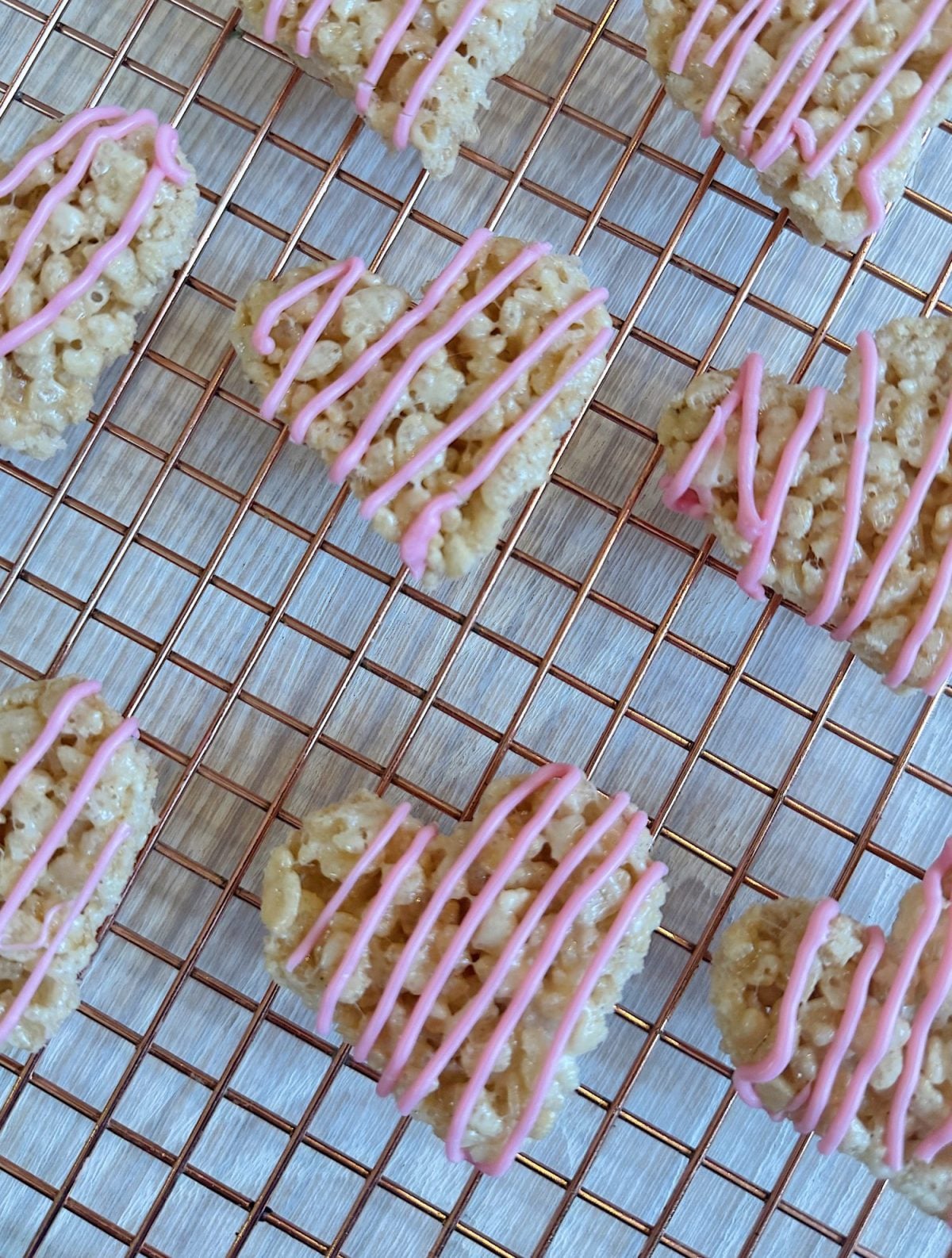 Heart-shaped rice krispie treats with pink icing drizzle on a wire cooling rack.