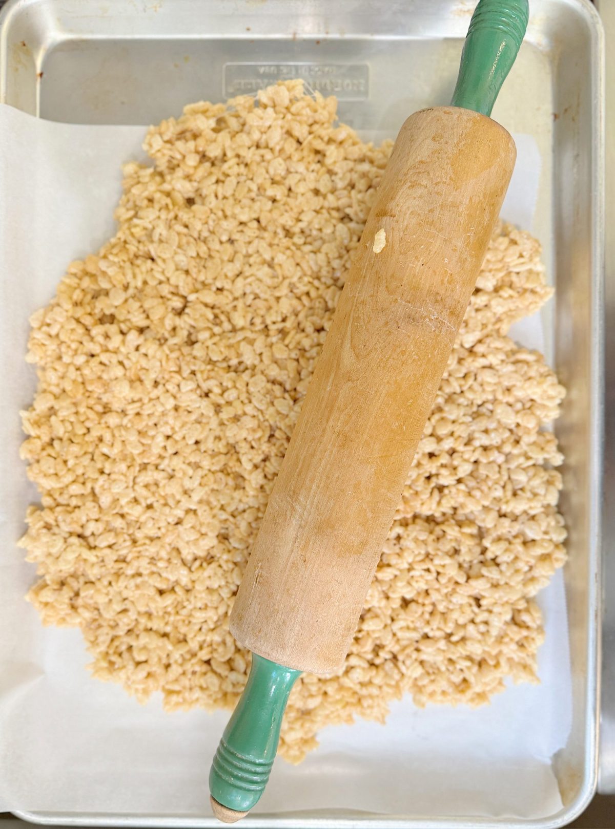 Rolling pin on parchment paper with rice cereal mixture on a metal baking sheet.