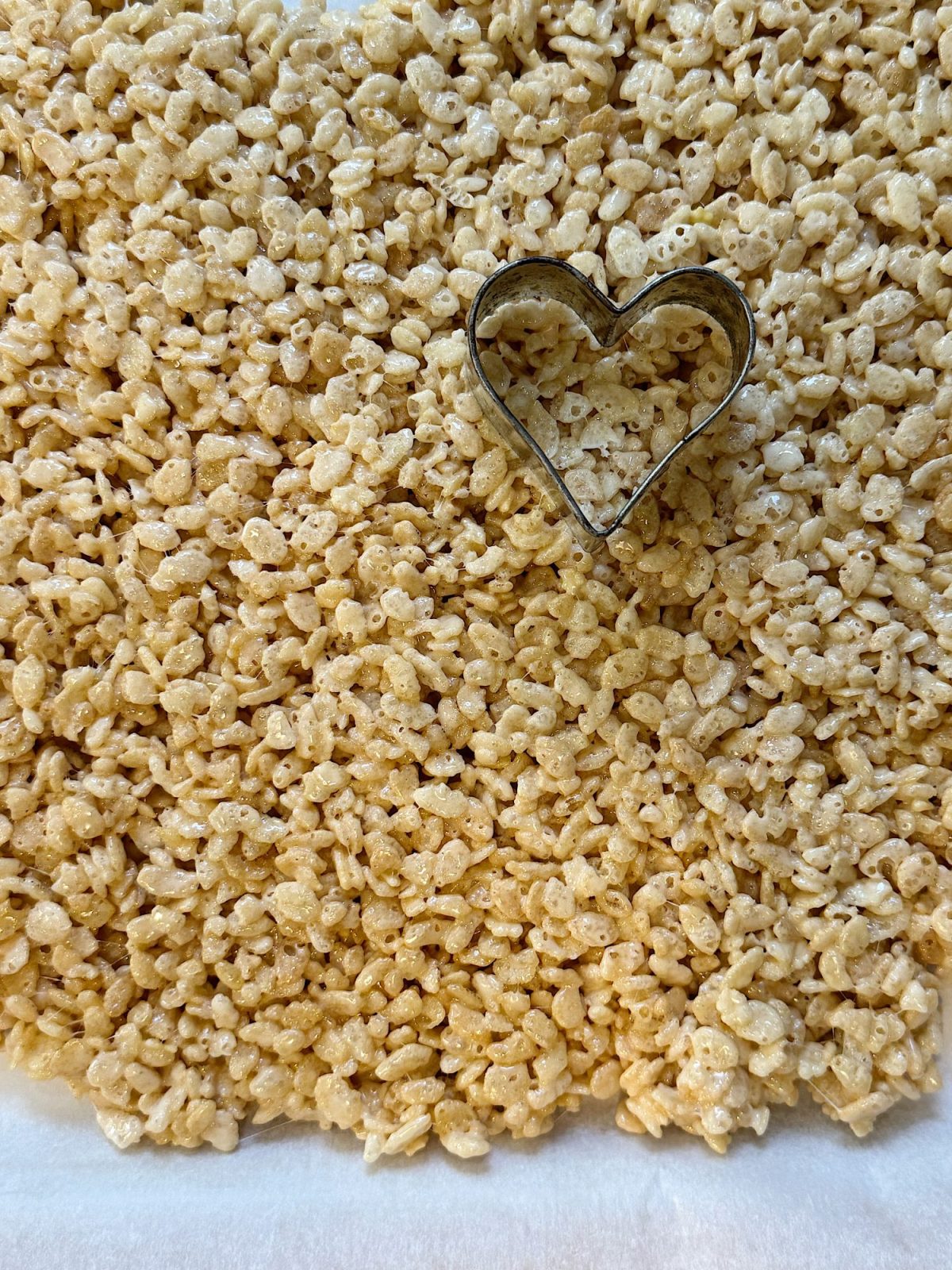 Heart-shaped cookie cutter on a sheet of rice krispie treats.