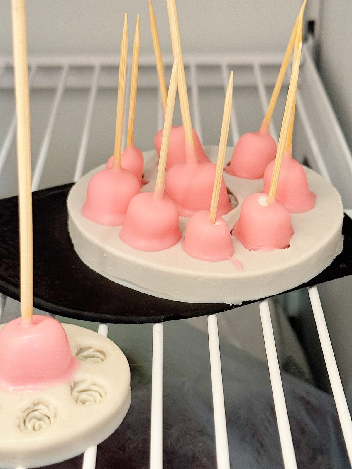 Pink dessert pops on skewers set in a silicone mold inside a refrigerator.
