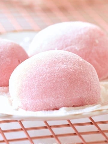 Close-up of three pink mochi on a plate with a dusting of powder.