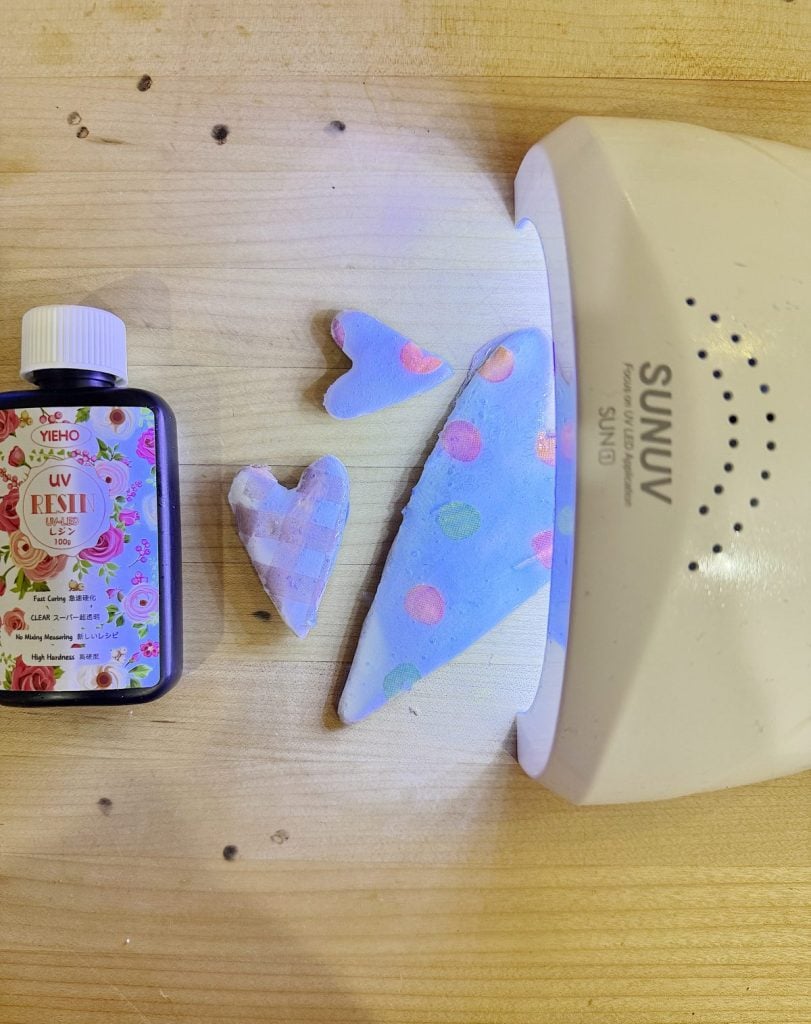 UV resin craft under curing lamp, with a decorated bottle nearby.