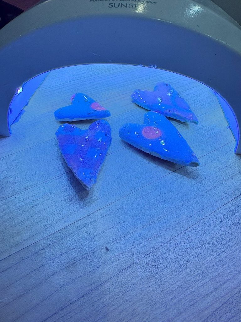 Blue heart-shaped clay pieces with pink dots under a UV light on a wooden surface.