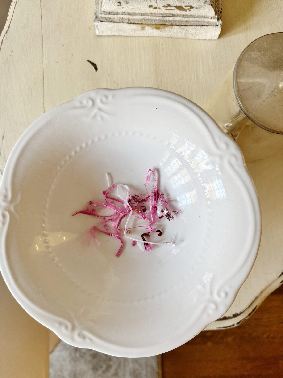 White bowl on a table with pink shavings and a reflective glass nearby.