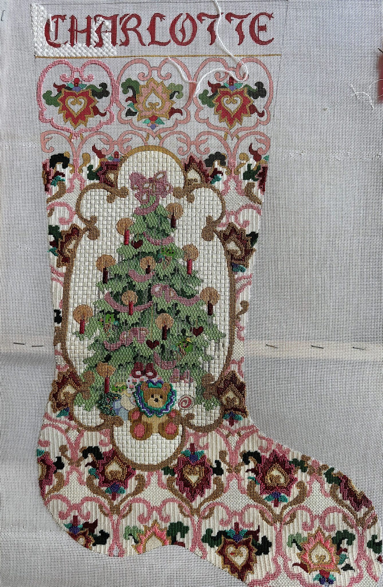 A decorated Christmas stocking with intricate patterns, featuring a central Christmas tree design and the name "Charlotte" embroidered at the top.