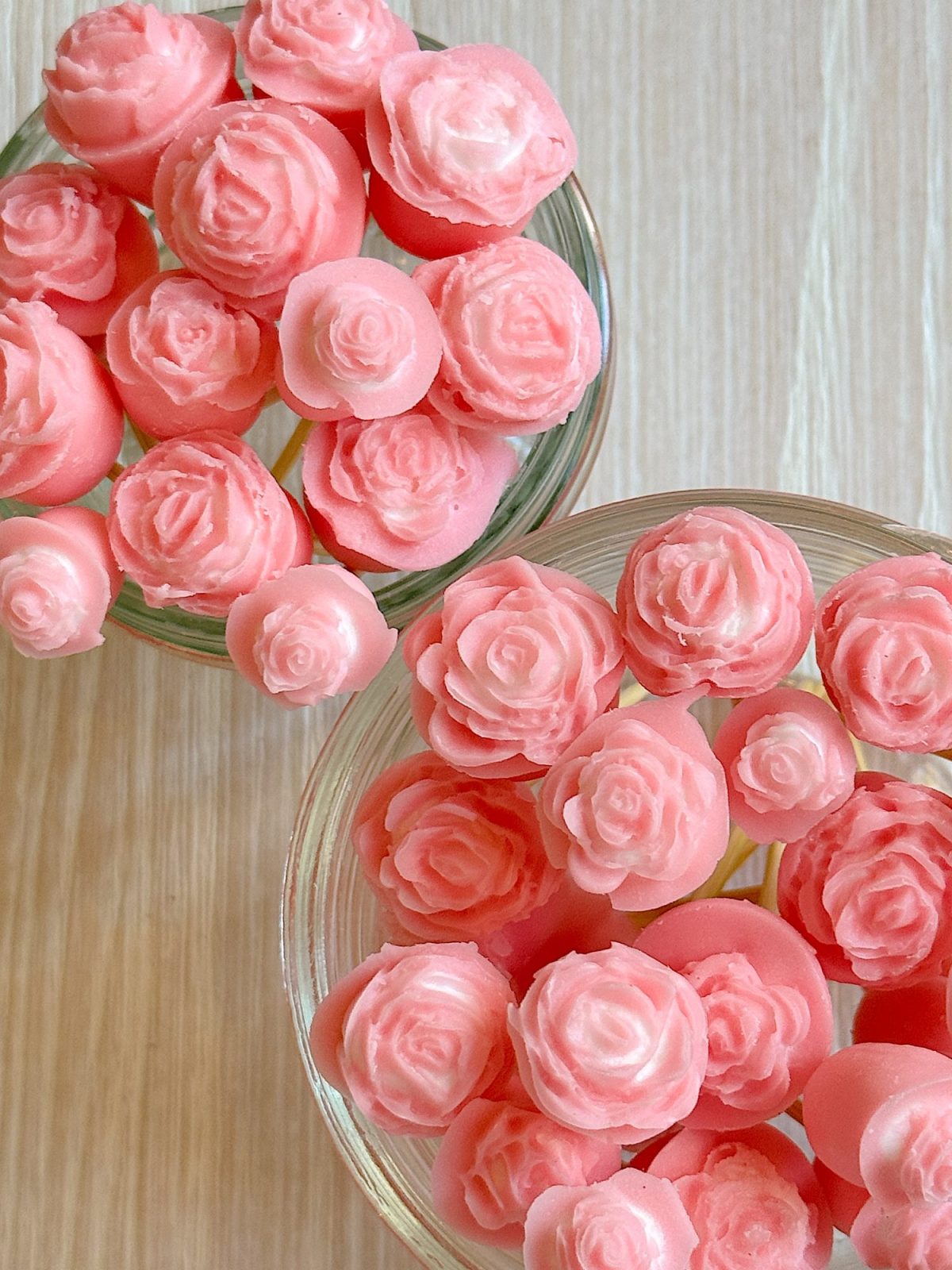 Two glass containers filled with pink rose-shaped wax melts on a light wooden surface.