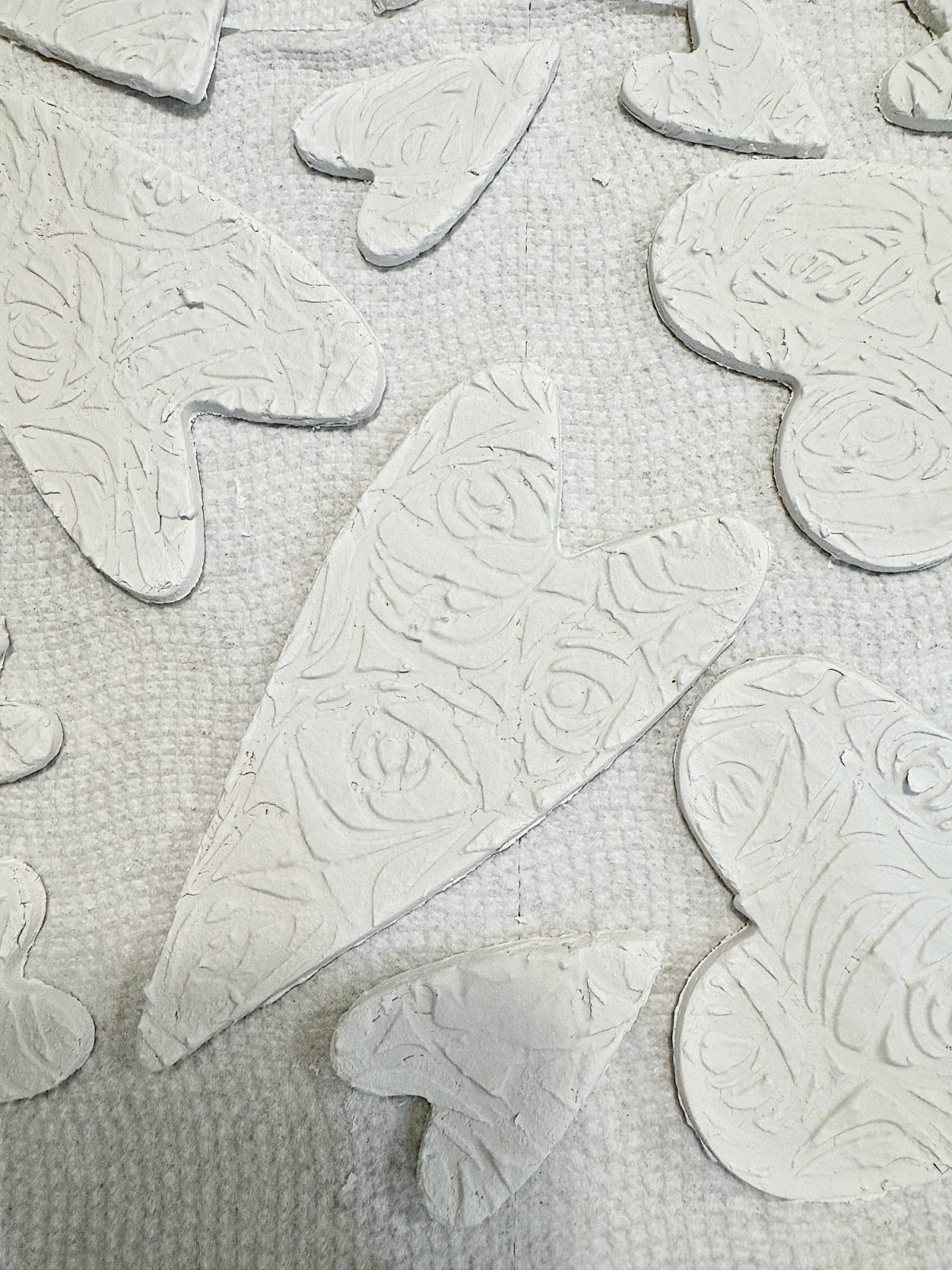 Various heart-shaped clay pieces with textured patterns lie on a textured surface, arranged in no particular order.