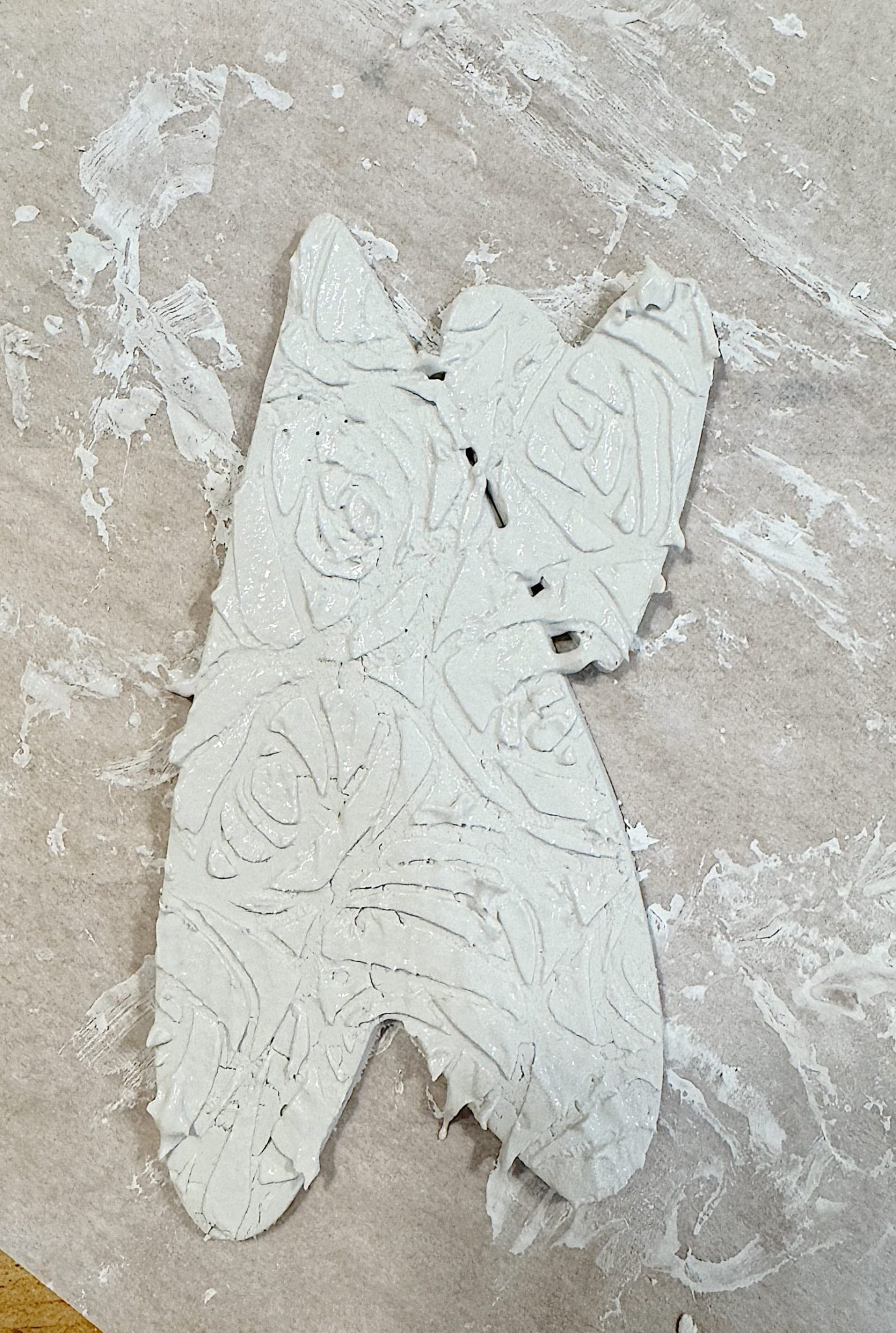 A clay butterfly sculpture with floral patterns, resting on parchment paper covered in white residue.
