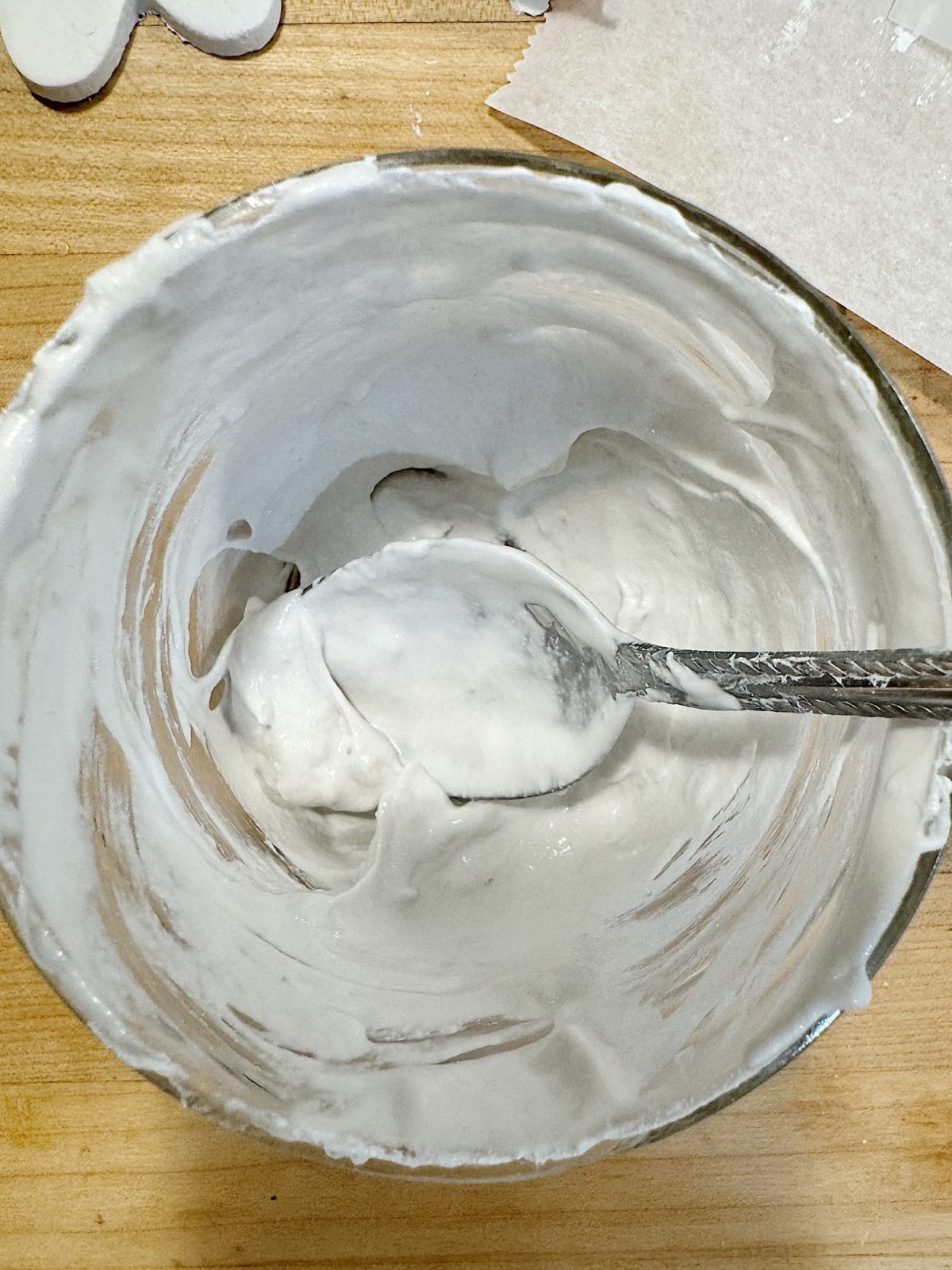 Bowl containing thick, white batter or paste with a spoon on a wooden surface.