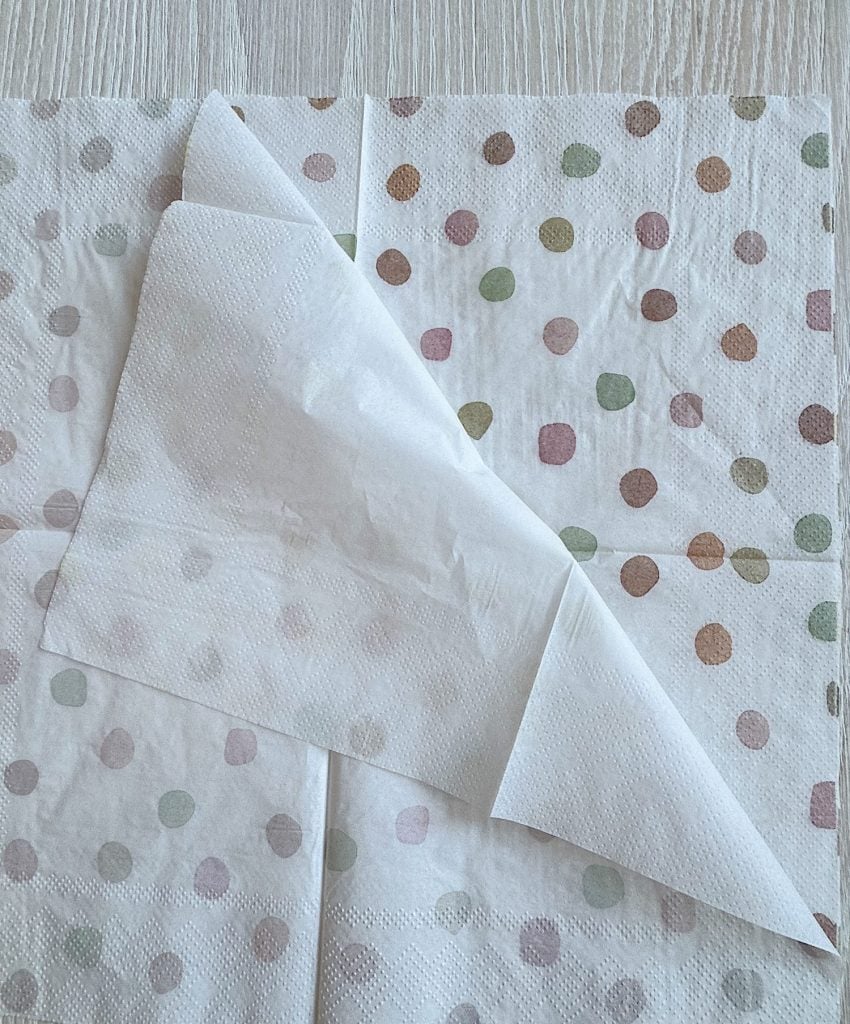 A white napkin with colorful polka dots and a folded corner sits on a light wooden surface.