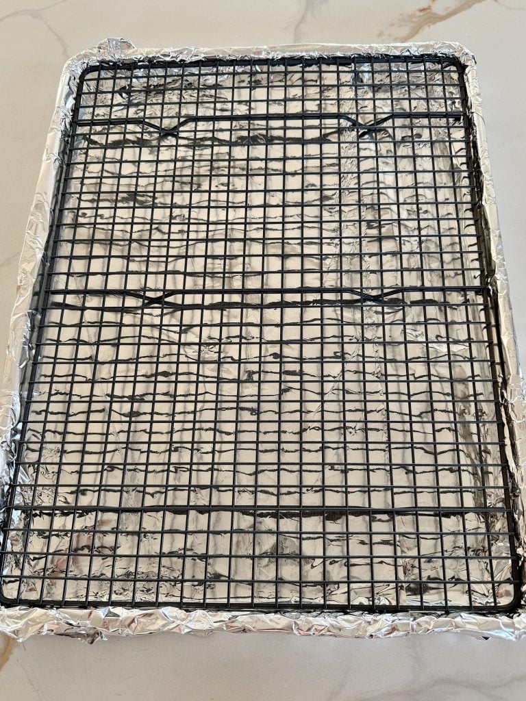 A wire cooling rack sits on a baking sheet lined with aluminum foil.