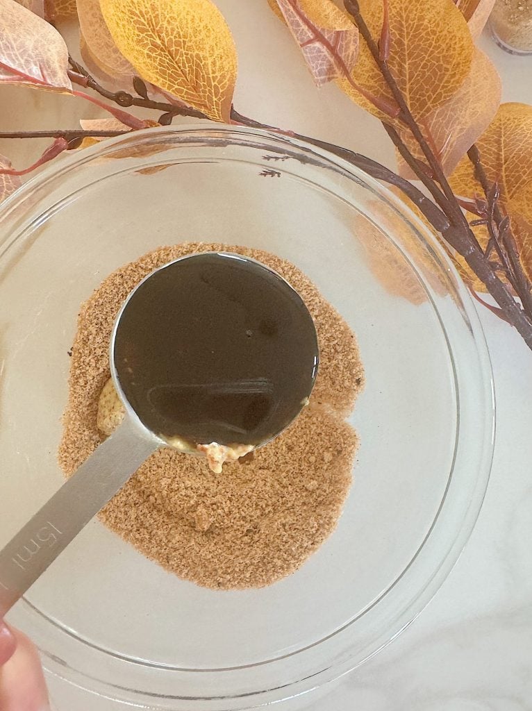 A measuring cup pours liquid into a bowl containing brown sugar, surrounded by autumn-themed decor.