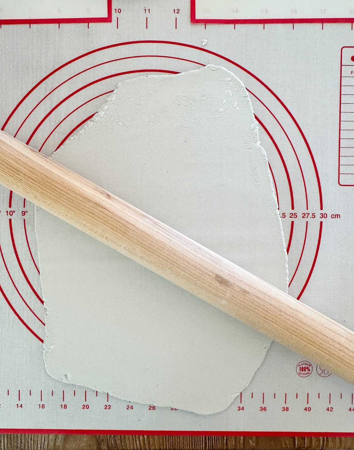 Wooden rolling pin on a gray non-stick baking mat with red measurement circles, flattening dough.