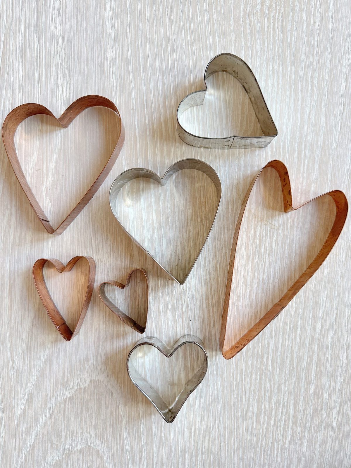 A collection of metal heart-shaped cookie cutters in various sizes on a light wood surface.