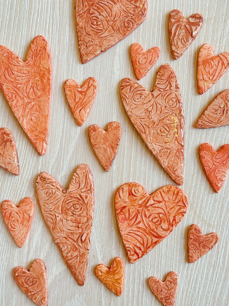 Various sizes of textured clay hearts in shades of orange are arranged on a light wooden surface.
