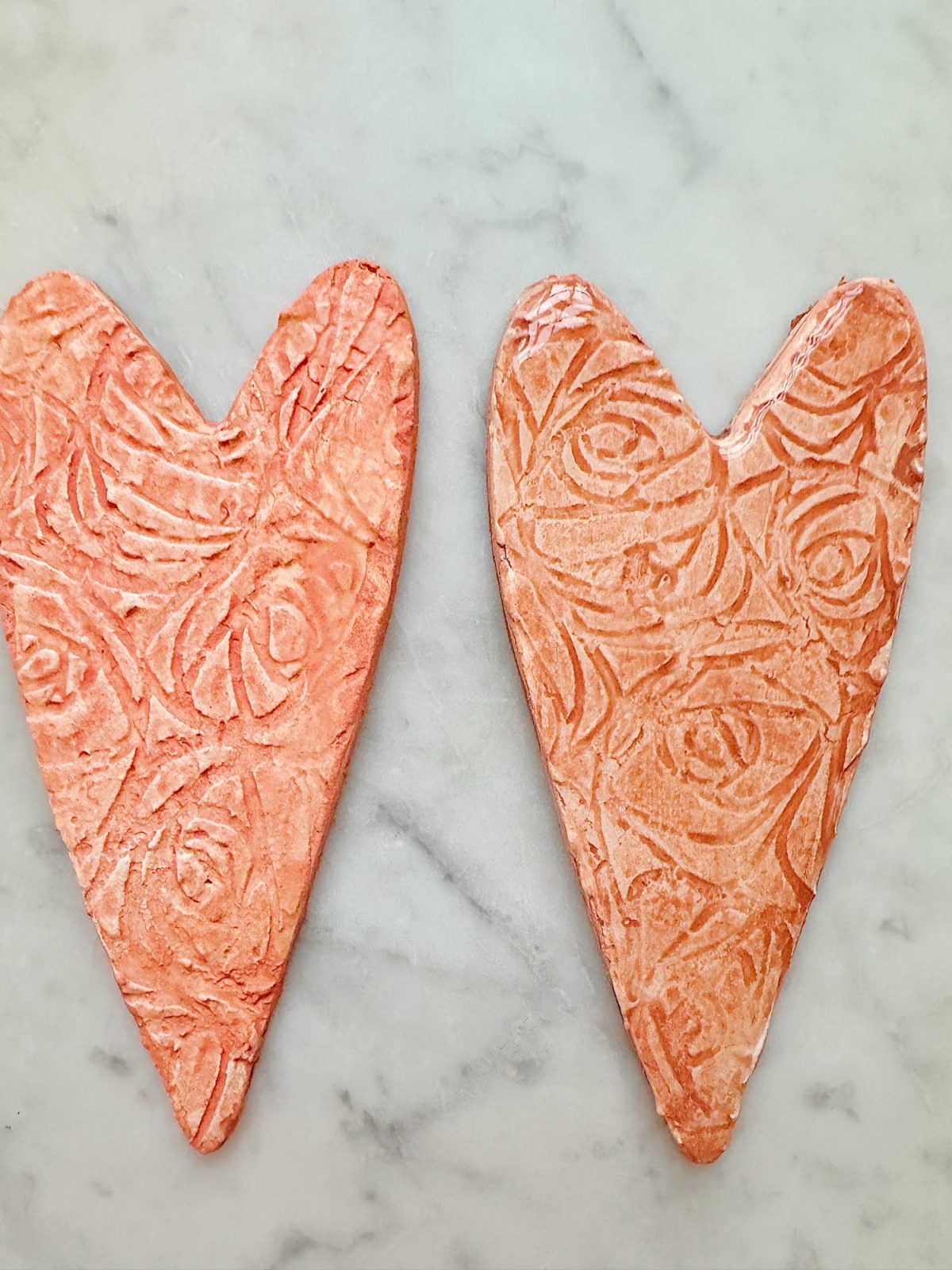 Two textured, pink heart-shaped objects with floral patterns on a marble surface.
