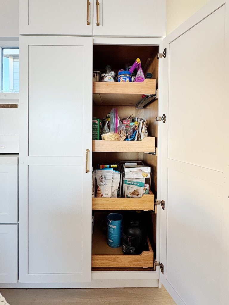 Open pantry cabinet with wooden pull-out shelves containing various food items and containers.