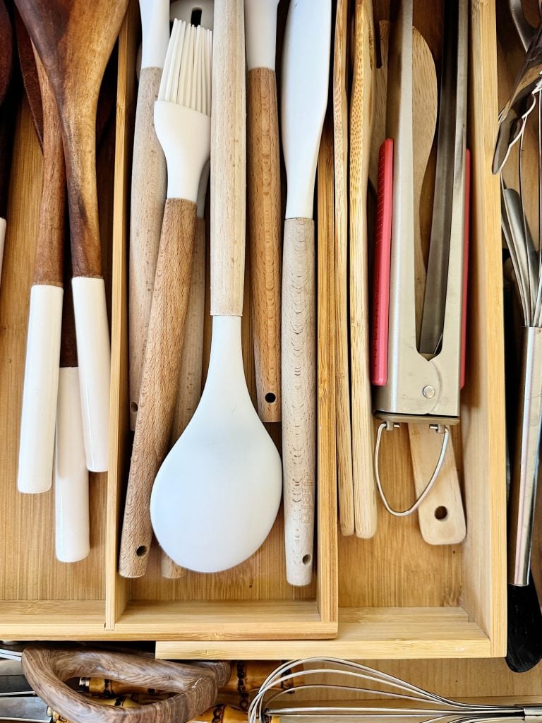 A drawer with organized kitchen utensils, including wooden spoons, a basting brush, a spatula, and tongs, on a wooden organizer.