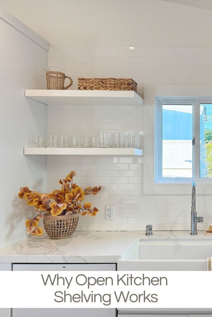 Minimalist kitchen with white shelves holding glasses and a basket, above a countertop with a wicker basket of brown flowers. A window is above the sink. Text: "Why Open Kitchen Shelving Works.