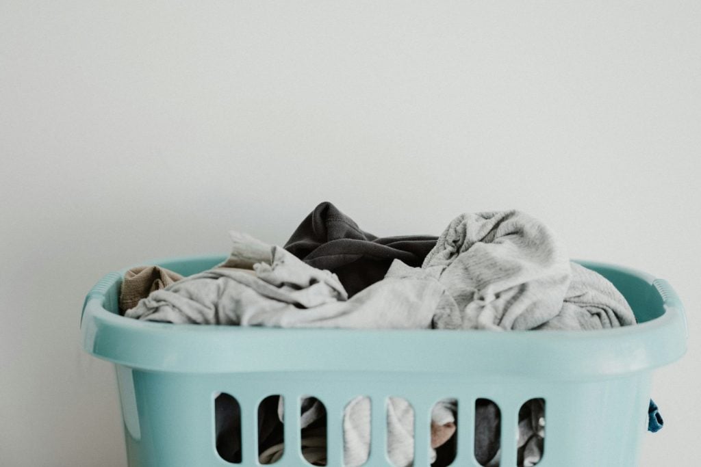 A light blue laundry basket filled with clothes against a plain white background.