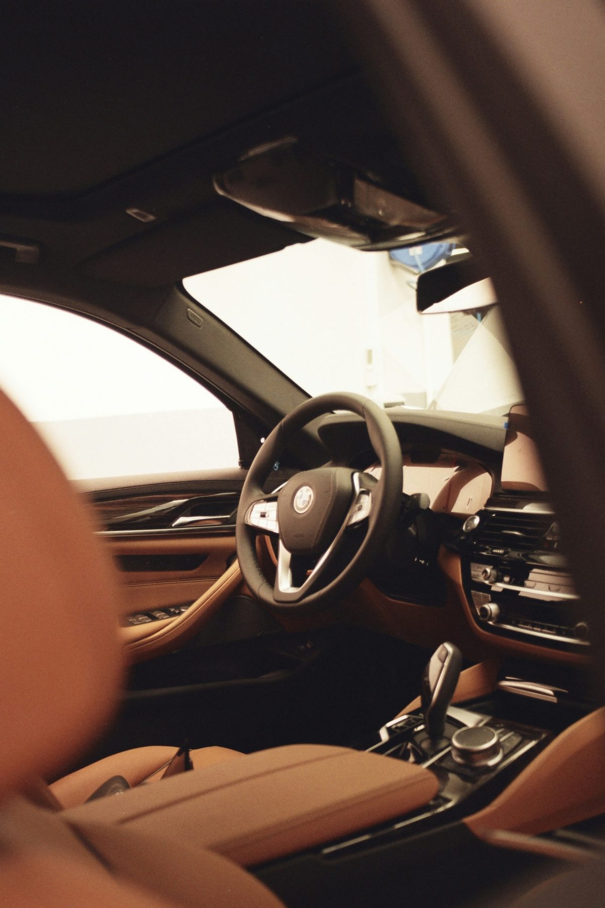 Interior view of a luxury car showing a steering wheel, dashboard, and brown leather seats.