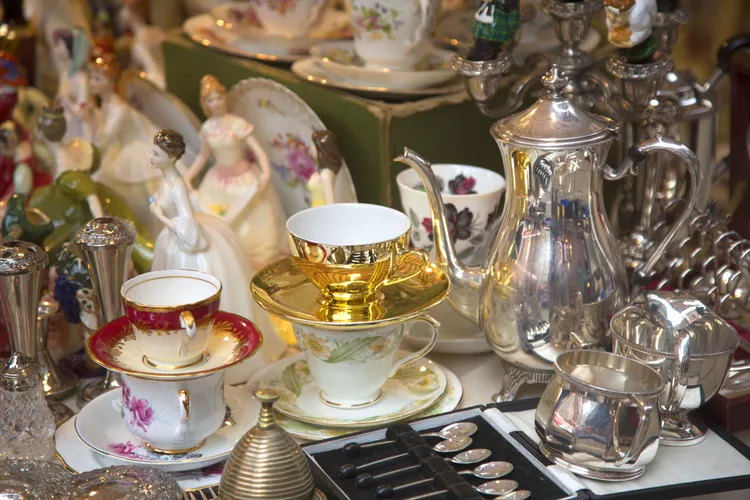 A collection of vintage porcelain teacups, metal teapots, and ceramic figurines displayed together, surrounded by small items like spoons and containers.