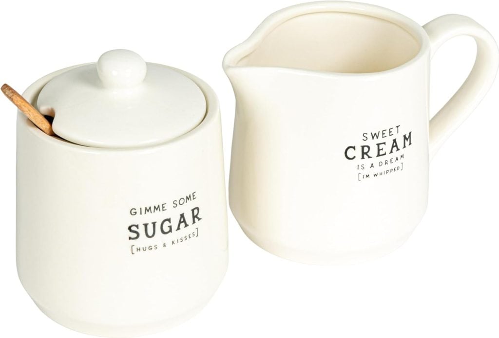 A white ceramic sugar jar with a lid and spoon sits next to a matching cream pitcher, both with black text and simple designs&mdash;perfect for serving alongside homemade cranberry orange scones.