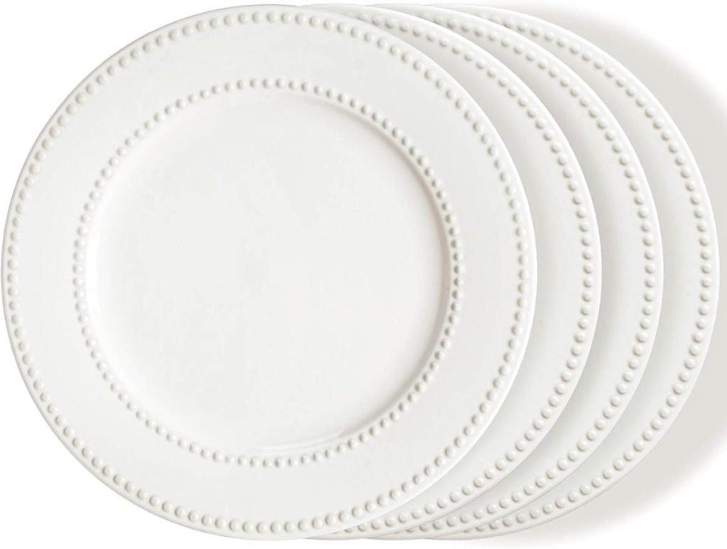 Four stacked white ceramic plates with a beaded rim design make an elegant addition to your dining room table decor, set against a crisp white background.