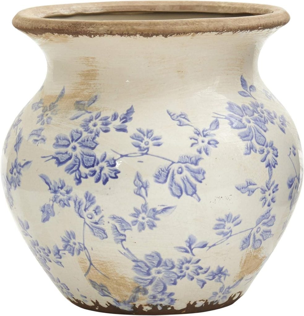 A round ceramic vase with a wide mouth, decorated with blue floral patterns and distressed, worn areas&mdash;perfect for displaying the best faux flowers in your home.
