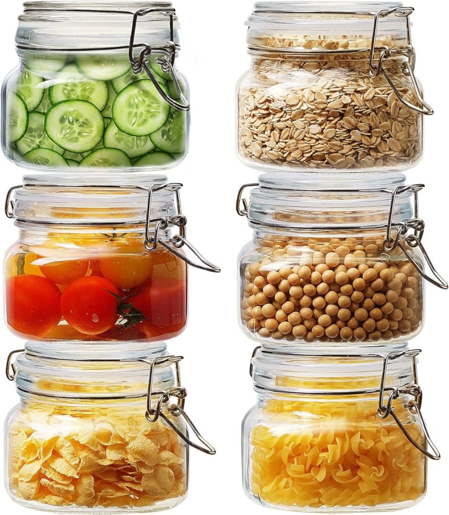 Six glass jars contain sliced cucumbers, oats, cherry tomatoes in liquid, chickpeas, cornflakes, and spiral pasta—perfect for pairing with your favorite salad dressing—arranged in two columns against a white background.