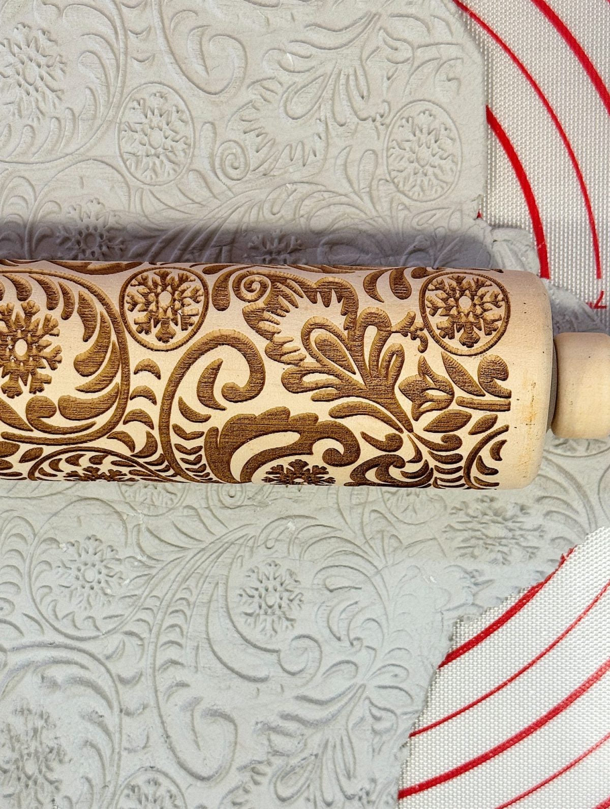 Close-up of a wooden rolling pin with intricate floral designs pressed into dough on a patterned baking mat.