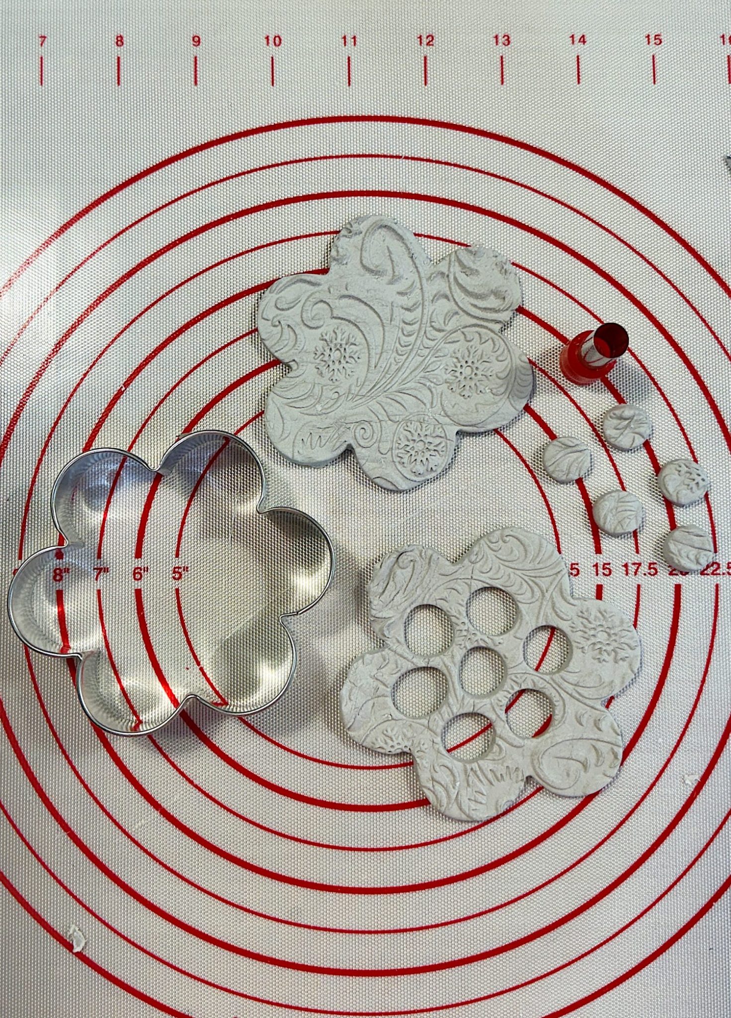 Embossed clay shapes and metal cutters on a red and white measuring mat.