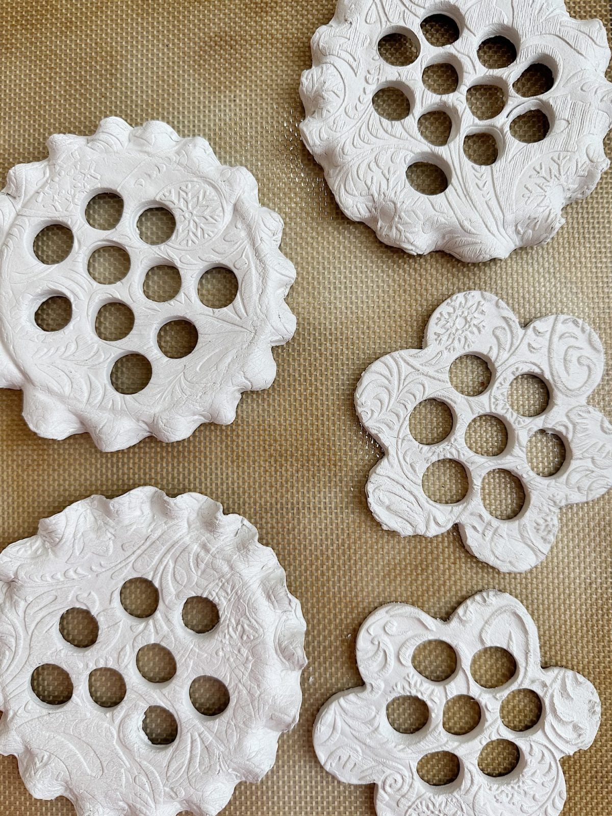 Textured, patterned clay ornaments with circular cutouts are arranged on a textured surface.