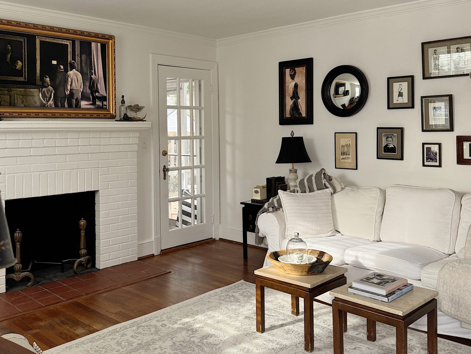 Living room with a white sofa, coffee table, and a white brick fireplace. Walls are adorned with various framed artworks, including a large painting above the fireplace.